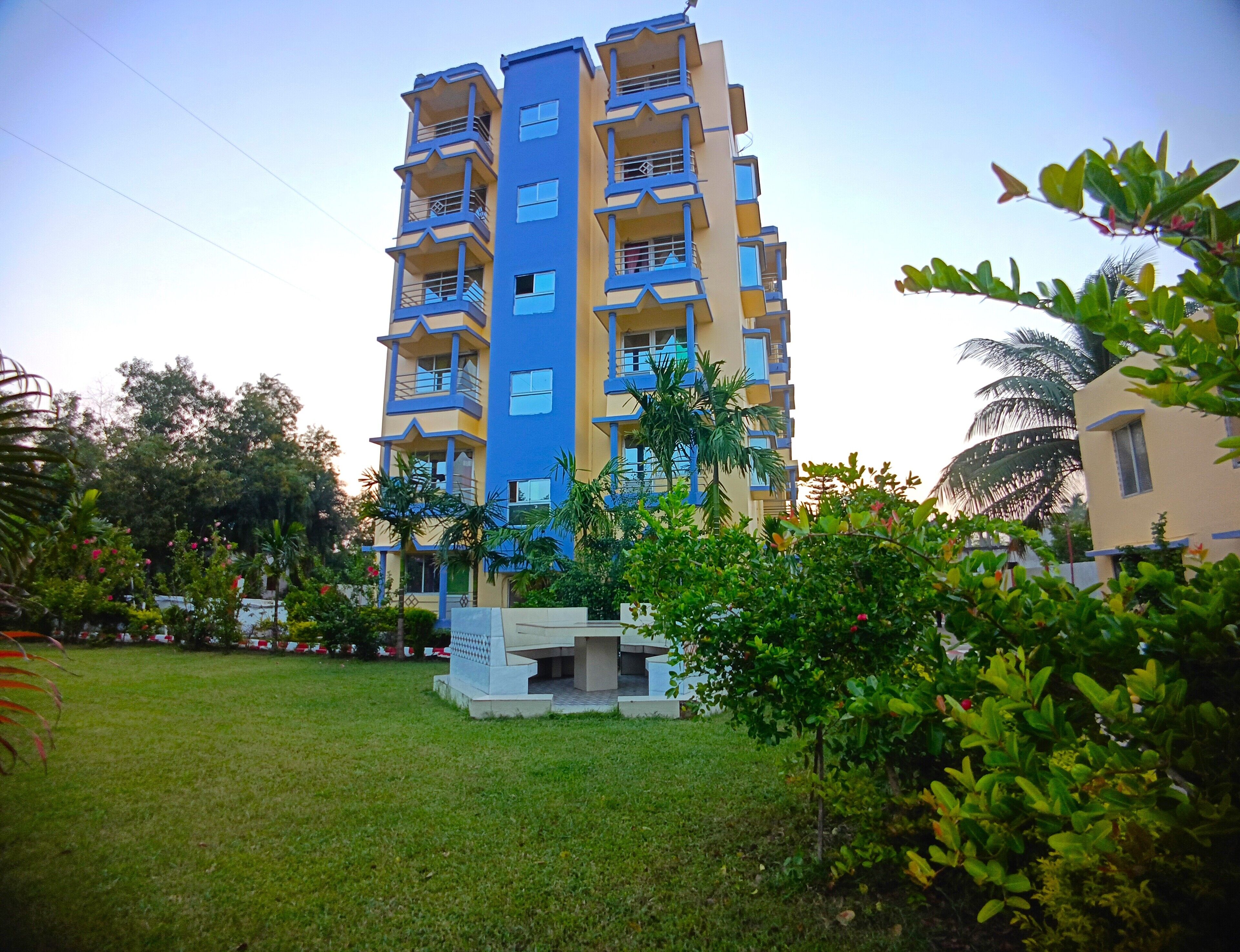 A multi-story residential building with balconies, surrounded by greenery and a well-maintained lawn.