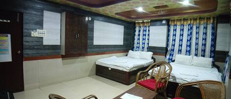 Habitación de hotel con dos camas individuales, una mesa de madera y dos sillas de mimbre con cojines rojos.