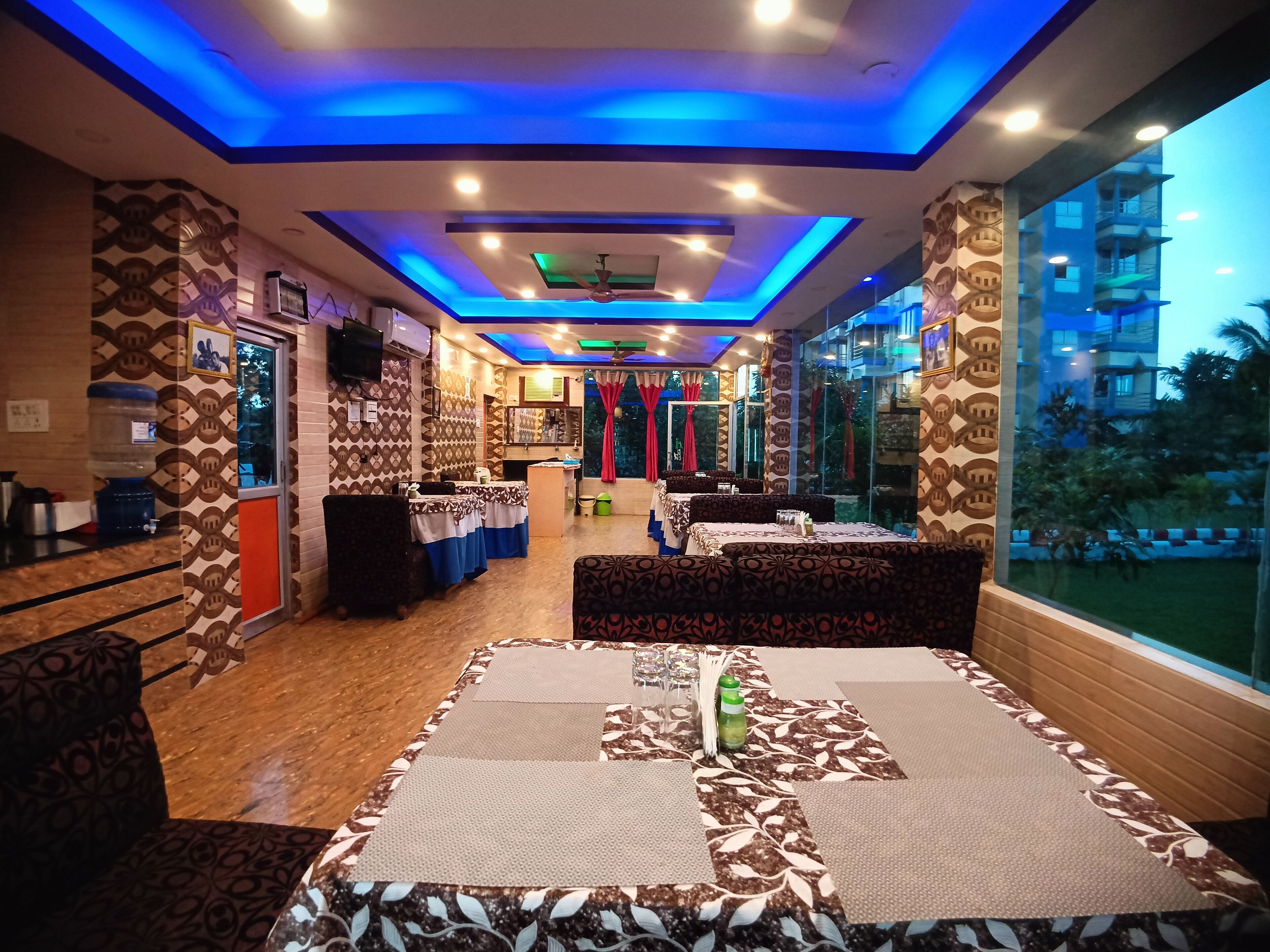 A restaurant with patterned walls, tables with tablecloths, and a view of a building outside.