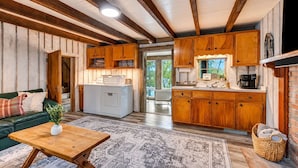 Een gezellig interieur van een chalet met een zithoek, houten kasten, een wasmachine en een keuken met een koffiehoek.