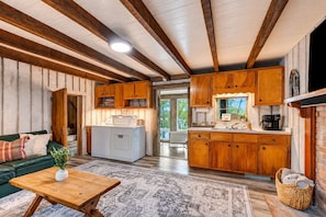 Un intérieur de chalet chaleureux comprenant un espace de vie, des meubles en bois, un lave-linge et une cuisine équipée d’un coin café.