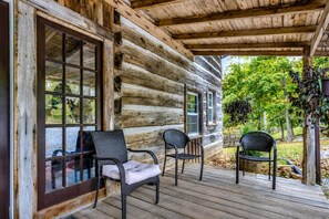Een vakantiehuis van hout met een veranda, twee rieten stoelen met kussens, en uitzicht op de groene omgeving.
