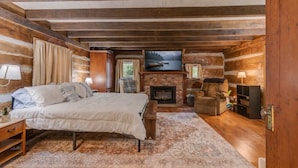 Een slaapkamer in een blokhut met een bed, open haard, televisie en uitzicht op de natuur.