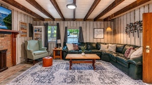 Een gezellige woonkamer met een houten plafond, een groene leren bank, een houten salontafel en een kamerkleed met een patroon.