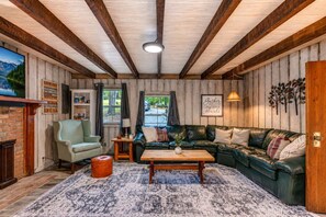 Un salon chaleureux avec un plafond en bois, un canapé en cuir vert, une table basse en bois et un tapis à motifs.