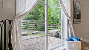 A room with a large window, a view of a forested area, a painting of a bull, and a laundry basket with clothes.