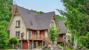 A two-story house with a red and beige exterior, a front porch with a staircase, and a small balcony.