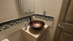 Une salle de bain avec un meuble-lavabo en bois, un lavabo en cuivre, un miroir et des toilettes.