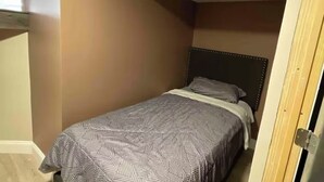 Une petite chambre étroite, avec un lit simple, une tête de lit en bois et un plafond en pente.