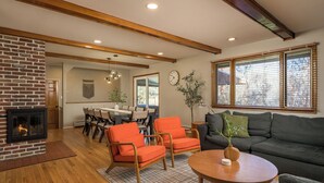 Ein Wohnzimmer mit Kamin, Holzbalken, einer Couch und orangenen Sesseln.
