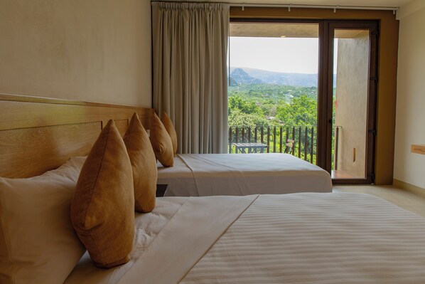 Ein Hotelzimmer mit zwei Betten, einem großen Fenster mit Blick auf eine gebirgige Landschaft und einem Balkon.