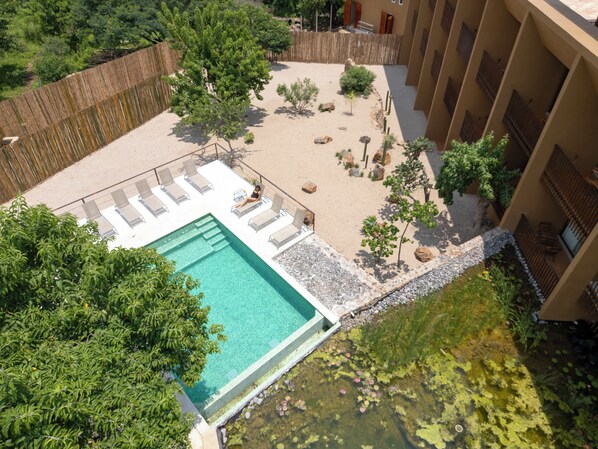 Una piscina en la azotea con vistas despejadas del paisaje circundante, que incluye un jardín cercado con diversas plantas y un edificio con balcones.
