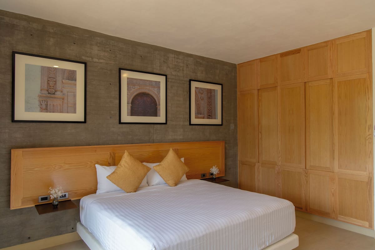 A bedroom with a large bed, wooden headboard, and a wardrobe. There are three framed pictures on the wall.