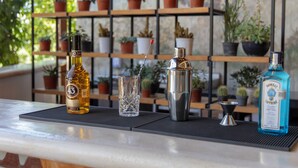 Eine Bar mit einer Whiskeyflasche, einem Glas, einem Shaker und einer Flasche blauer Spirituose auf einer Matte.