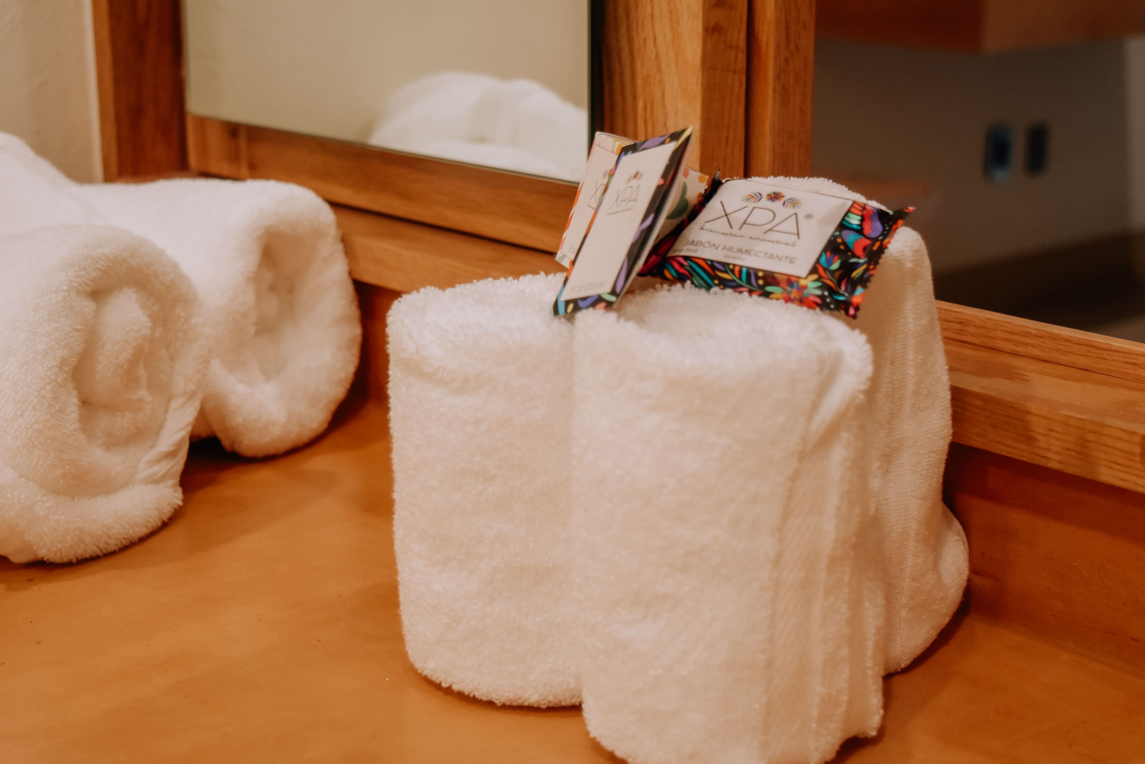 A hotel room with a wooden floor, a mirror, and two white towels placed on a white textured surface.