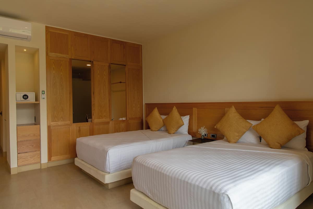 A hotel room with two beds, wooden wardrobe, and a small bedside table.