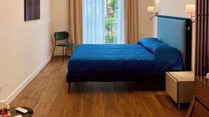 Een moderne slaapkamer met een bed, een stoel, een nachtkastje en een raam met gordijnen.