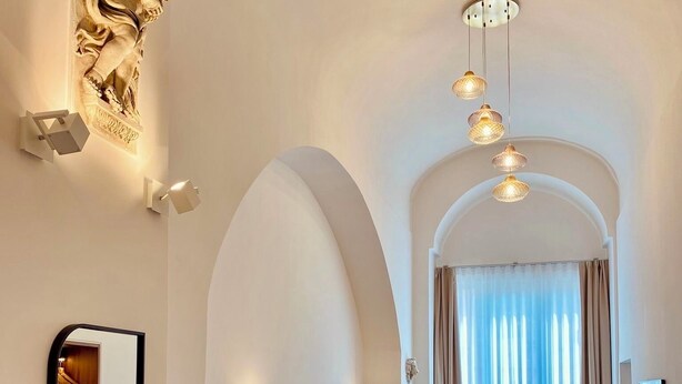 Een hotelkamer met een bed, een klein tafeltje, een spiegel en een kledingkast. Er zijn gewelfde plafonds en een kroonluchter.