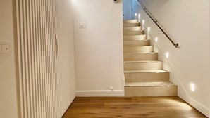 Een moderne trap met houten treden en een metalen leuning, die uitkomt op een plateau met een blauwe wand en een witte radiator.
