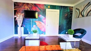 Una sala moderna con un gran mural abstracto, un televisor de pantalla plana, una puerta blanca y un sillón azul.