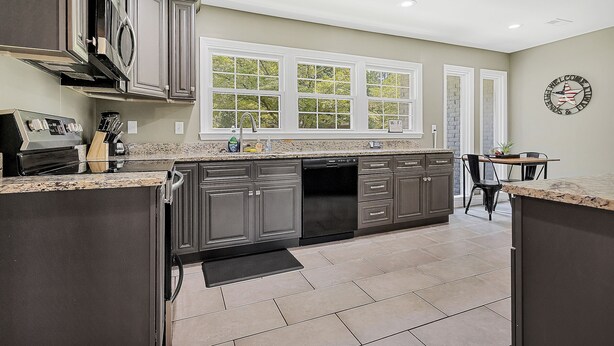 A kitchen with dark cabinets, a dishwasher, a microwave, and a large window. - American Retreat (Huntsville)