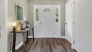 A hallway with a white door, a dark wooden console table with a lamp, and a framed picture. - American Retreat (Huntsville)