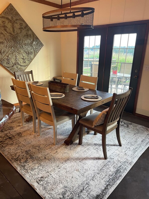 A dining area with a wooden table and chairs, a decorative wall piece, and a view through a glass door. - Relaxing rustic charm in Stillwater, OK - open floor plan & nice patio! (Stillwater)