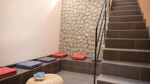 A staircase with a stone wall and a small seating area with cushions and a woven stool. - Vila Mira Mar (São Vicente)