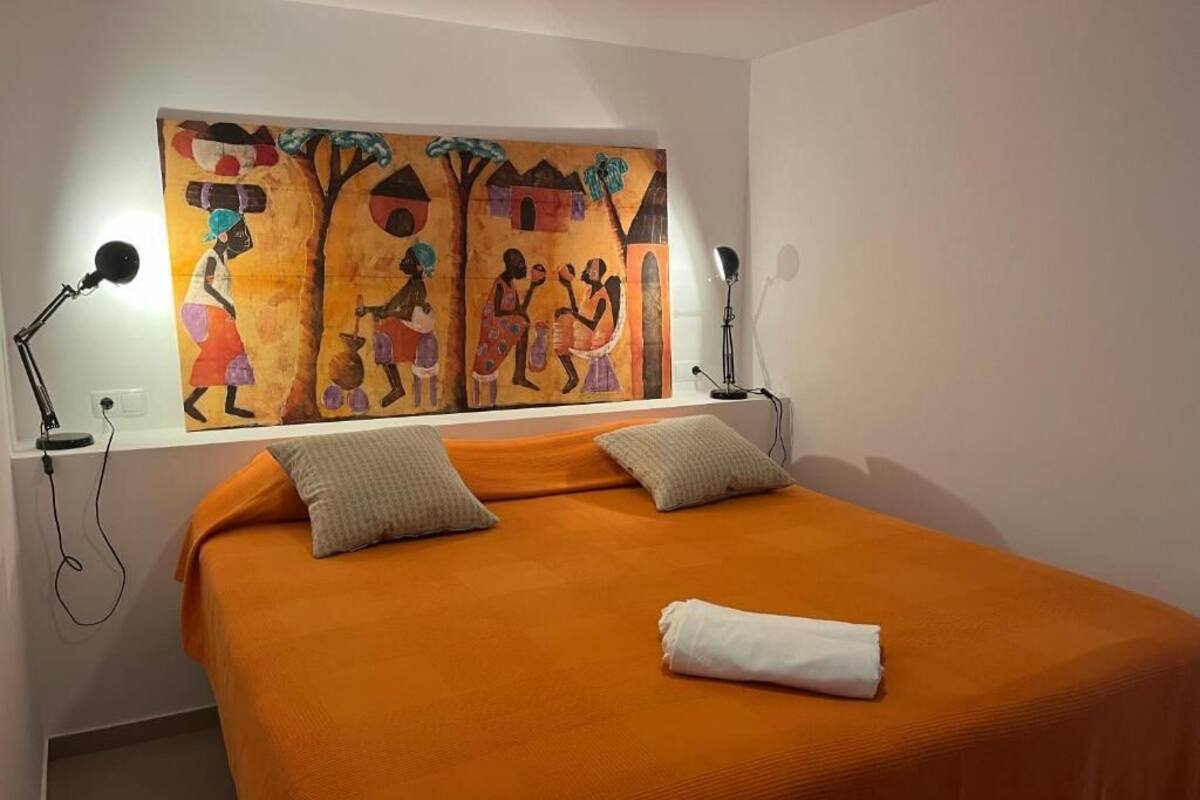 A room with a large bed, two bedside lamps, a painting on the wall, and a folded towel on the bed.