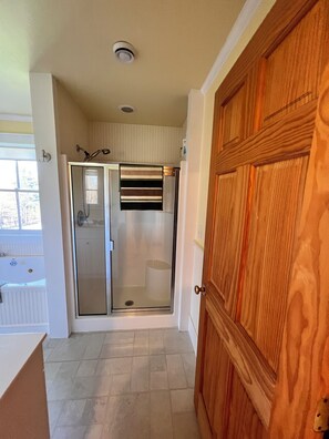 A bathroom with a glass shower enclosure, a wooden door, and a tiled floor.