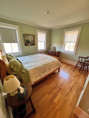 Une chambre à coucher comprenant un lit, une commode, une chaise et une fenêtre avec des stores.