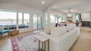Un salon spacieux avec un canapé blanc, un fauteuil bleu et un tapis coloré. Une grande fenêtre offre une vue sur l’extérieur.