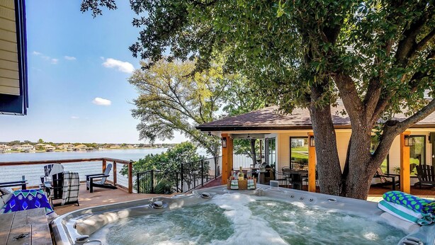 Un bain à remous sur une terrasse, avec vue sur un lac, entouré d’arbres et de mobilier d’extérieur.