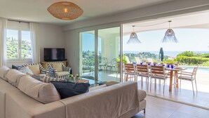 Un salon moderne avec un canapé, un téléviseur et un coin repas offrant une vue sur la mer.