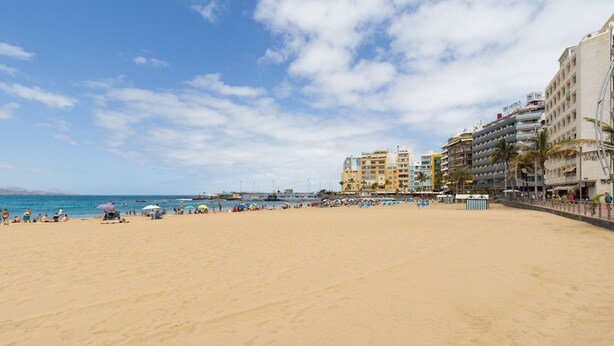 Una playa con una hilera de edificios de varios pisos, incluyendo un hotel con un cartel.