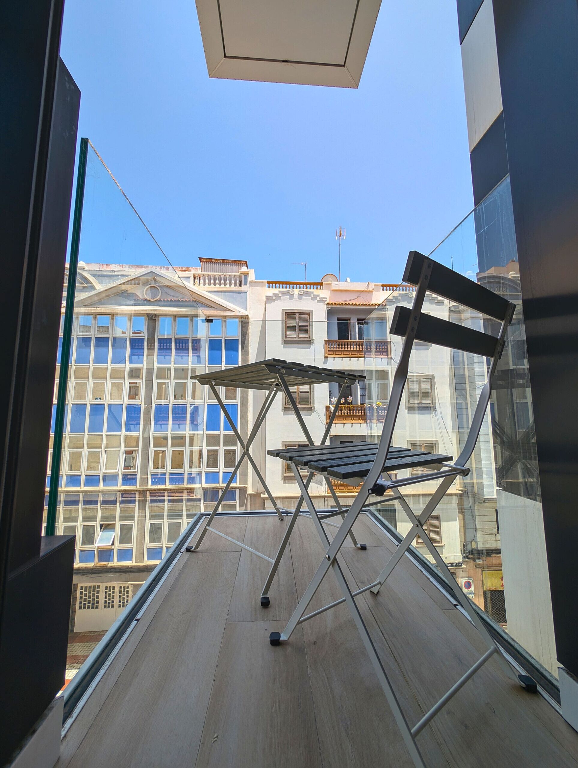 Ein Balkon mit einem Klappstuhl aus Metall und Glasgeländer.
