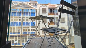 Un balcón con una silla plegable de metal y barandilla de vidrio.