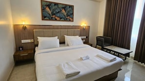 A hotel room with a large bed, two bedside tables, a chair, a painting on the wall, and a window with curtains.