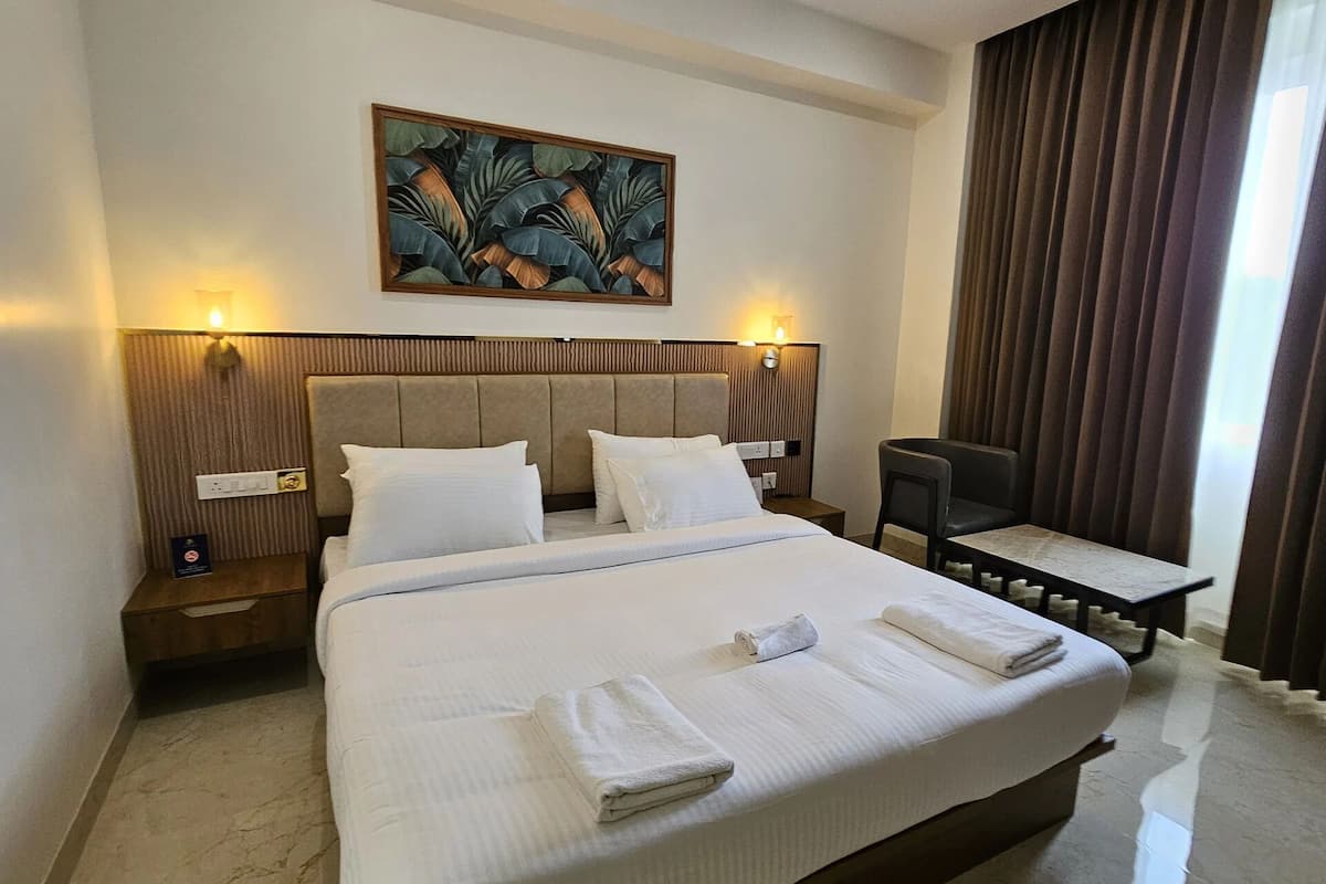 A hotel room with a large bed, two bedside tables, a chair, a painting on the wall, and a window with curtains.