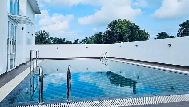 A modern pool with clear blue water, surrounded by a white wall and a clear sky.