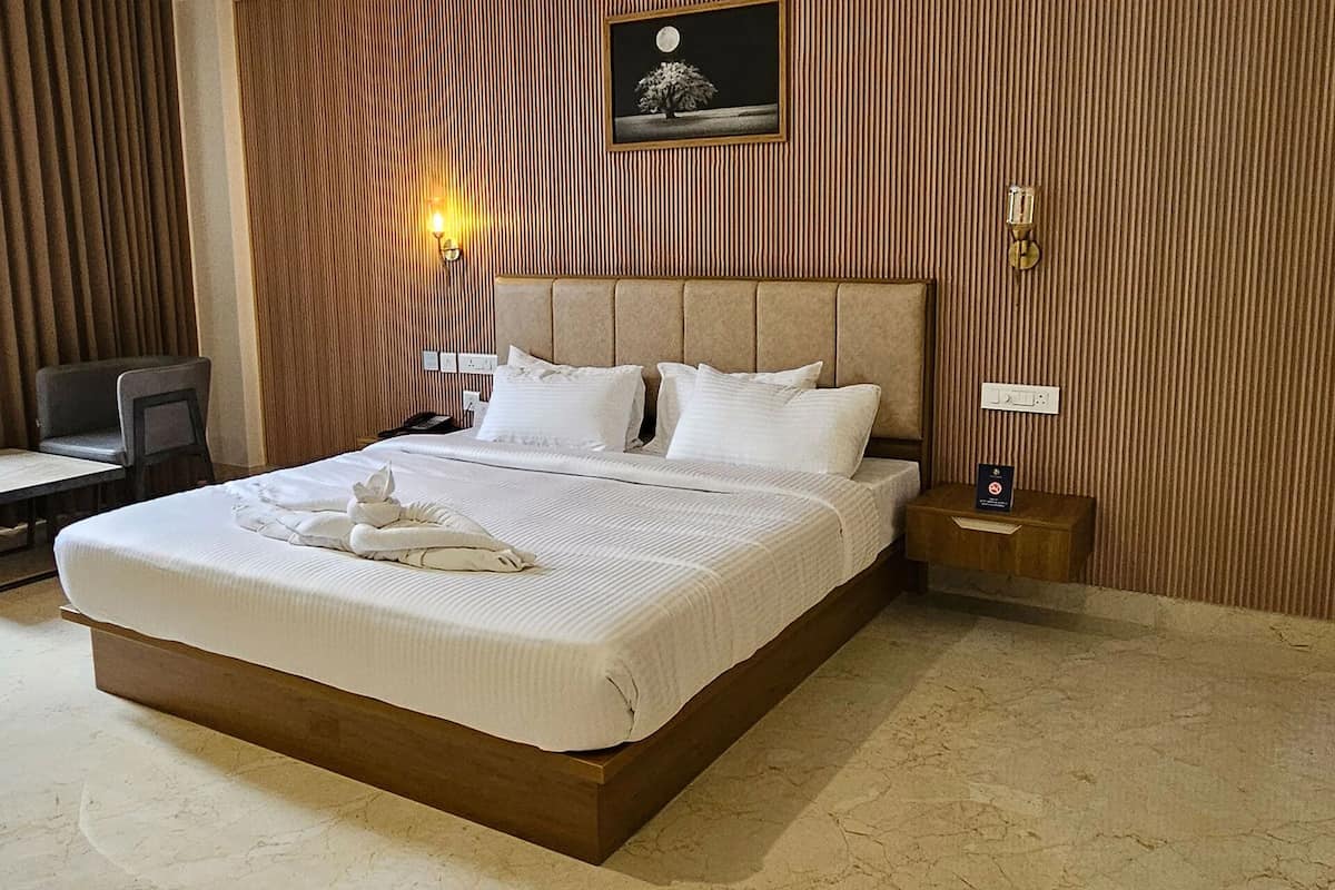 A neatly made bed with white linens and a towel, a bedside table with a phone, and a wall-mounted picture of a tree under a moon.