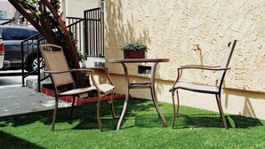 A small outdoor seating area with two chairs and a table, a potted plant, and a car parked nearby.