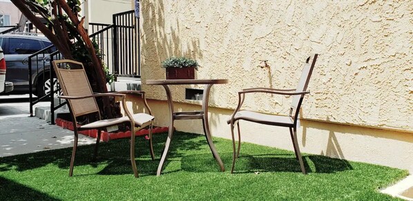 A small outdoor seating area with two chairs and a table, a potted plant, and a car parked nearby.