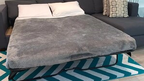 A room with a grey sofa, a grey sofa bed, a patterned rug, and a painting on the wall.
