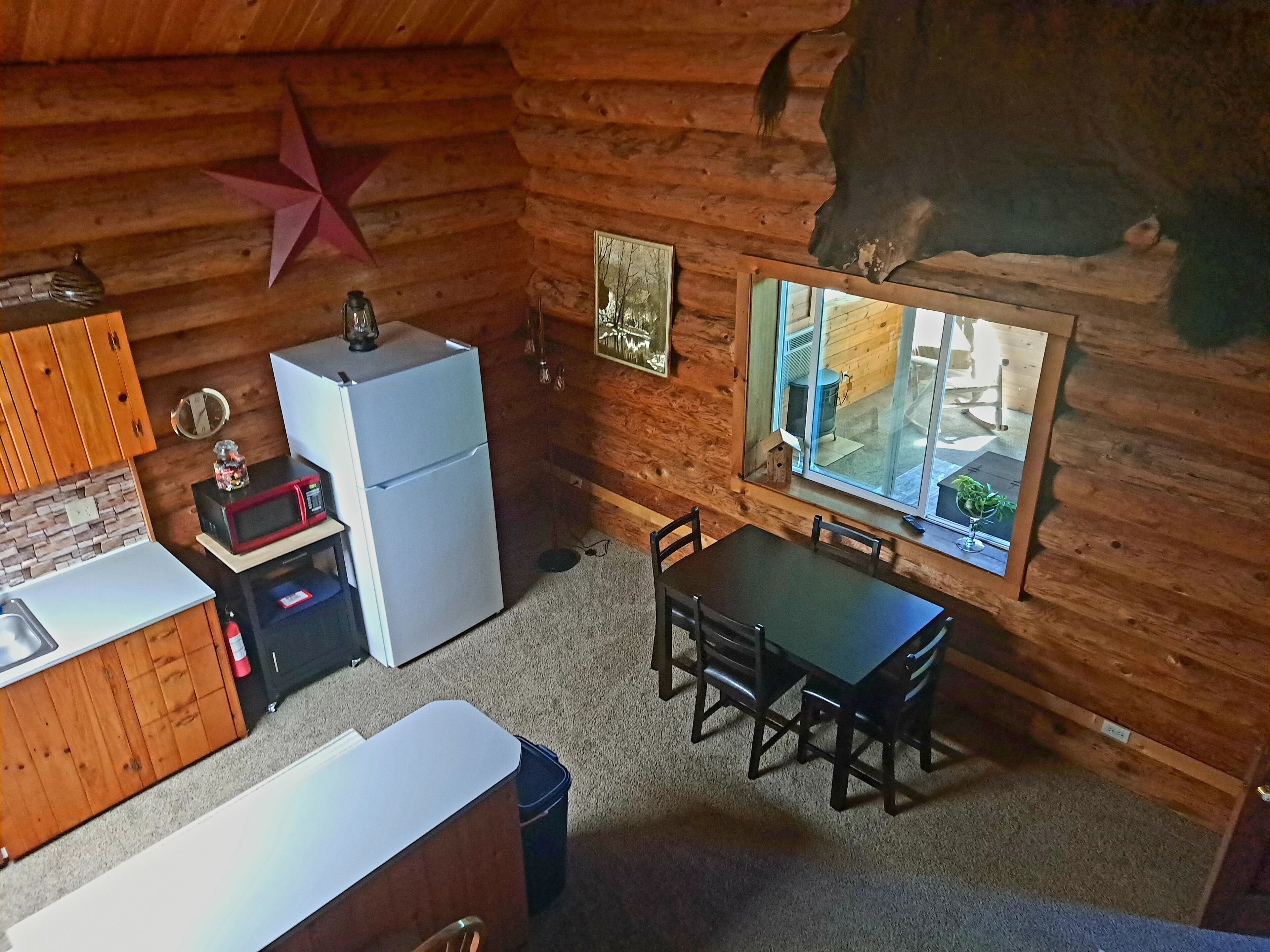 L’intérieur chaleureux d’un chalet, avec un revêtement mural en bois, un réfrigérateur, un four à micro-ondes, une table à manger avec des chaises et une fenêtre donnant sur l’extérieur.