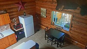 L’intérieur chaleureux d’un chalet, avec un revêtement mural en bois, un réfrigérateur, un four à micro-ondes, une table à manger avec des chaises et une fenêtre donnant sur l’extérieur.
