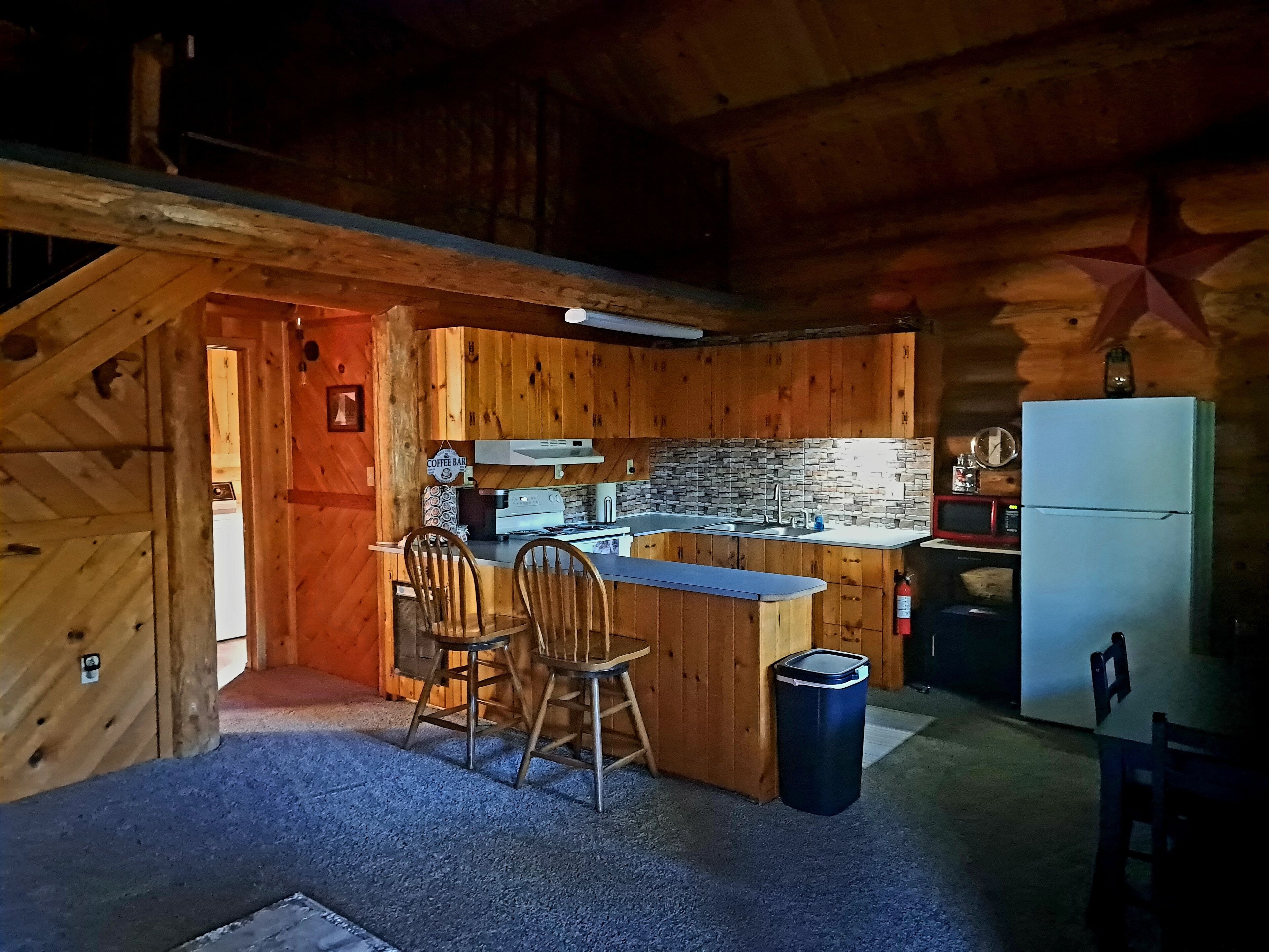 A cozy cabin-style kitchen with wooden walls, a stone backsplash, and a small dining area with two chairs and a table.