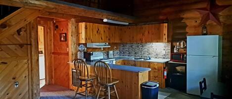 A cozy cabin-style kitchen with wooden walls, a stone backsplash, and a small dining area with two chairs and a table.