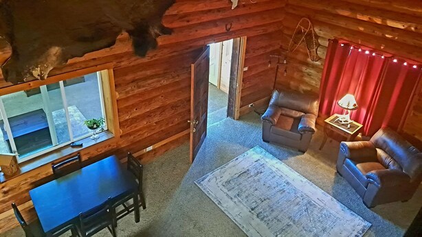 A rustic cabin interior with a dining area, a living room with a leather sofa, and a ceiling-mounted deer head. - Cozy Middle Fork Cabin.                      
    Across from Clearwater River  (Kamiah)