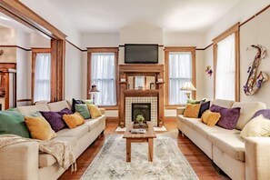A living room with a fireplace, two sofas, a coffee table, and a television. - Central Location Historic Grandeur (Mobile)